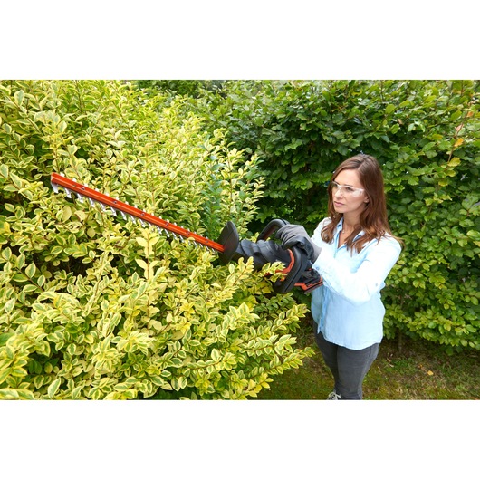 Person using BLACKDECKER BCASK891D hedge trimmer to trim green bushes outdoors.