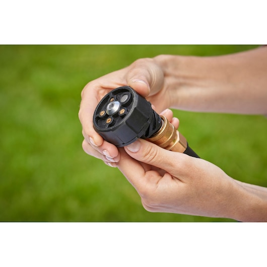 Close-up of two hands adjusting the nozzle of a garden hose, with a blurred green grass background.