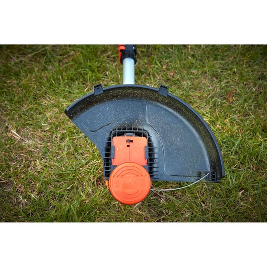 BLACKDECKER BCSTA536B grass trimmer head with black debris guard and orange spool, photographed on grass.