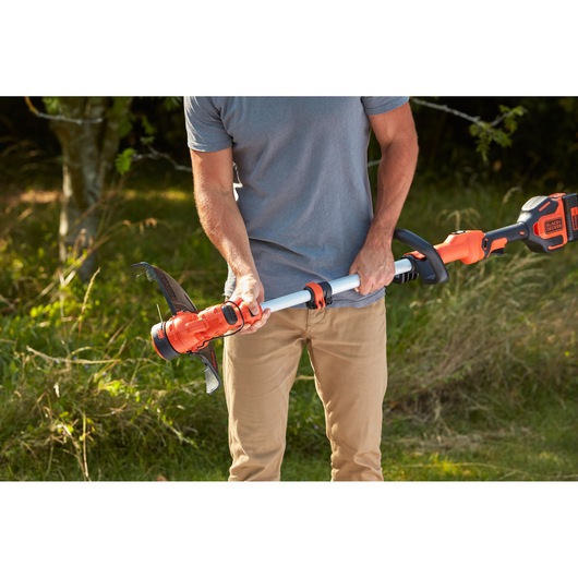 Photo of person holding BLACKDECKER BCSTA536B orange cordless grass trimmer in a garden.