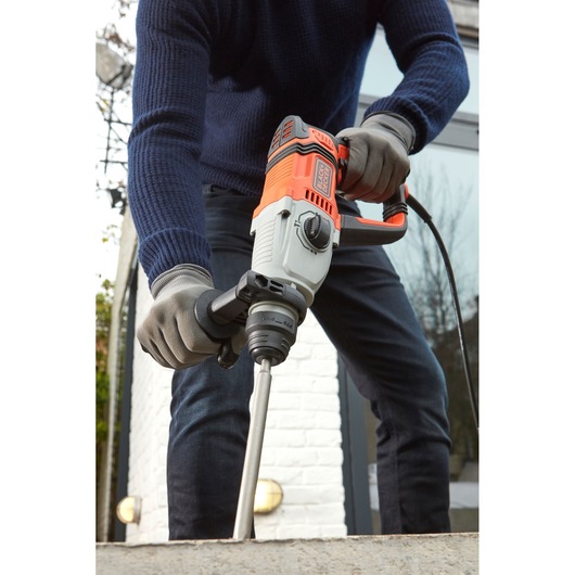 BLACKDECKER BEHS02K rotary hammer drill in use, orange and grey design, held by person wearing gloves.