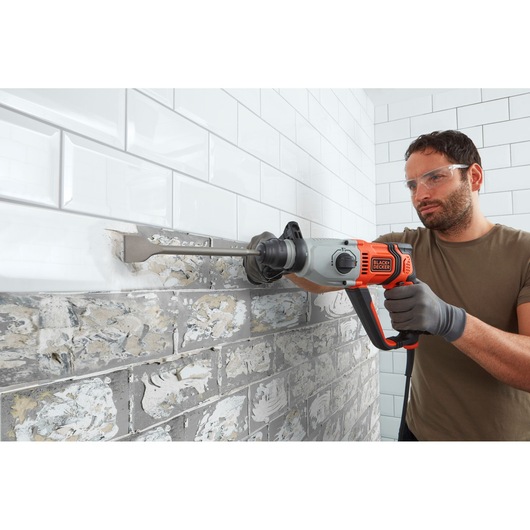 BLACKDECKER BEHS02K hammer drill removing tile from wall, side view, orange and gray tool.