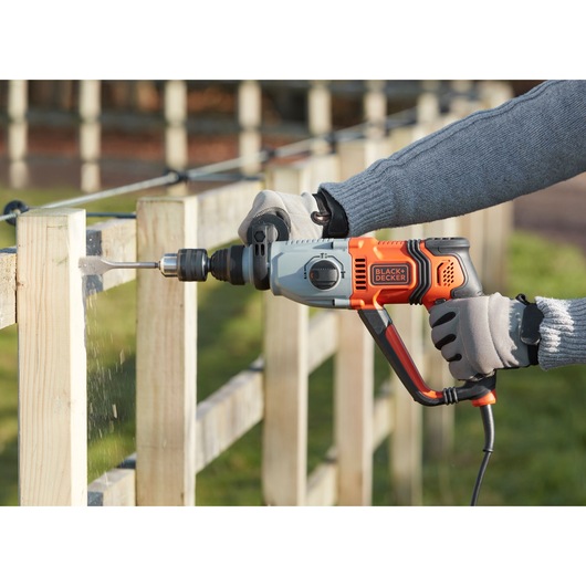 Photo of BLACKDECKER BEHS02K corded hammer drill in use drilling into a wooden fence outdoors.