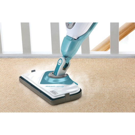 A BLACK+DECKER steam mop is shown cleaning a carpeted floor beside a white railing.
