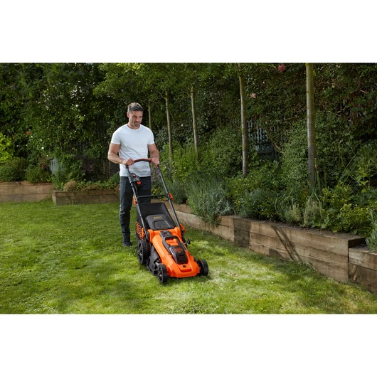 BLACKDECKER CLMA4820L2 orange cordless lawn mower on grass beside raised garden beds, outdoor use.