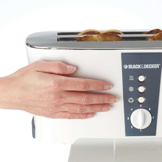 Photo of BLACK+DECKER toaster ET124 in white with hand touching side and toast inside, front angle.