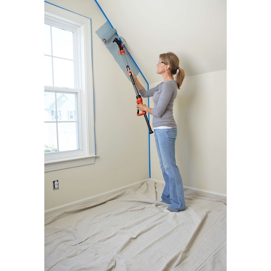 Pivoting rapid roller being used by a person to paint edge of wall.