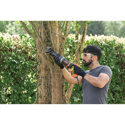 Reciprocating saw with Removable branch holder being used by a person to remove branch.