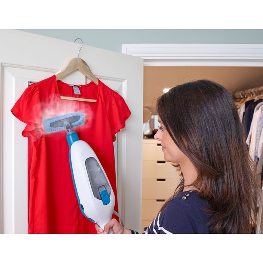 BLACKDECKER FSMH13E10 handheld steam cleaner used to freshen a red dress on a hanger in a closet setting.