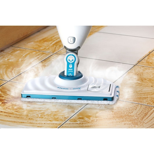 A close-up of a BLACK+DECKER steam mop cleaning dirty tile flooring. The mop emits steam as it glides over the tiles, removing dirt and leaving a clean surface behind.