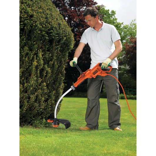 BLACKDECKER GL8033 grass trimmer used outdoors by person trimming lawn edge near hedge.