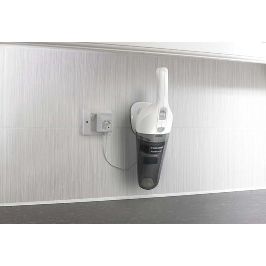 A BLACK+DECKER handheld vacuum cleaner mounted on a wall charging station in a modern, light-colored room.