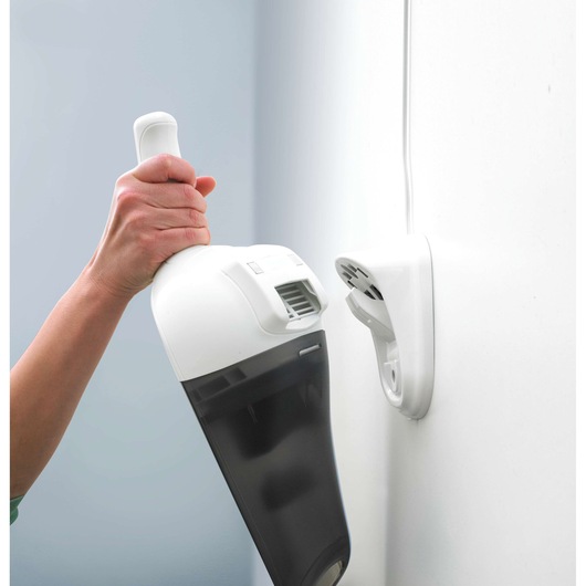 A hand is holding a BLACK+DECKER handheld vacuum cleaner near a wall-mounted charging station.