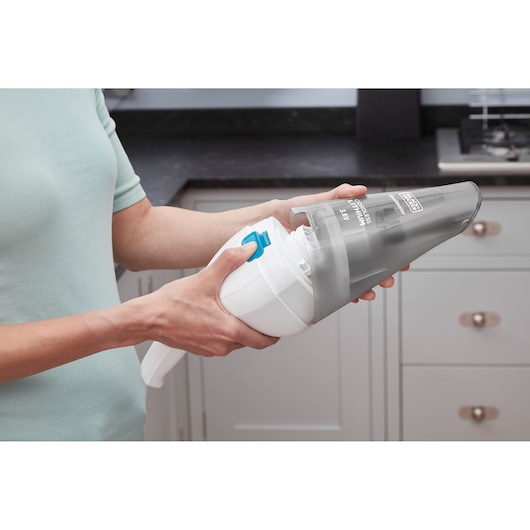 A person is holding and cleaning a BLACK+DECKER handheld vacuum cleaner in a kitchen.
