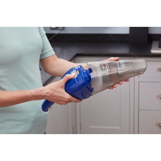 A person holding and opening a BLACK+DECKER NVC115WA handheld cordless vacuum cleaner in a kitchen setting.
