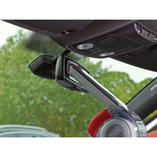 A BLACK+DECKER handheld vacuum cleaner (model PV1200AV) is being used to clean a car interior, targeting the area around the rearview mirror and windshield.