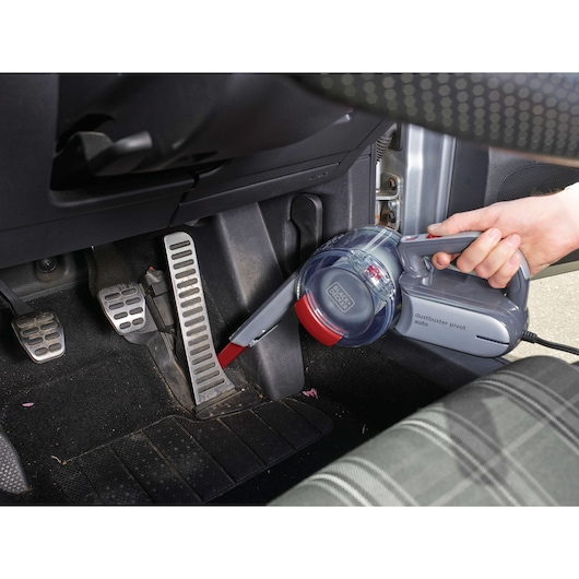 A person uses a BLACK+DECKER dustbuster pivot auto handheld vacuum cleaner to clean the area around the car pedals.