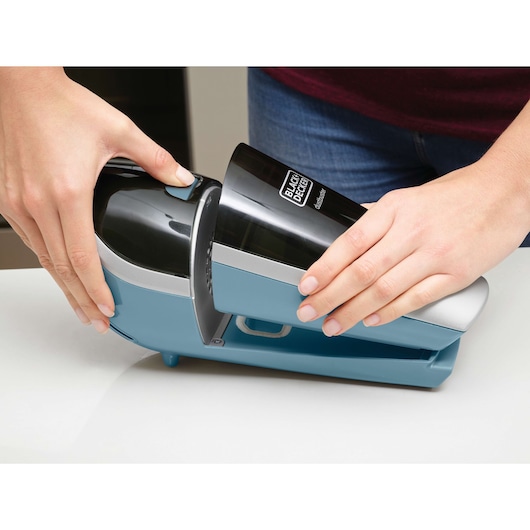 Close-up of hands removing the BLACK+DECKER handheld vacuum from its charging base.