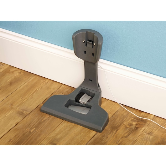 A Black+Decker vacuum cleaner charging station mounted on a wooden floor against a blue wall.