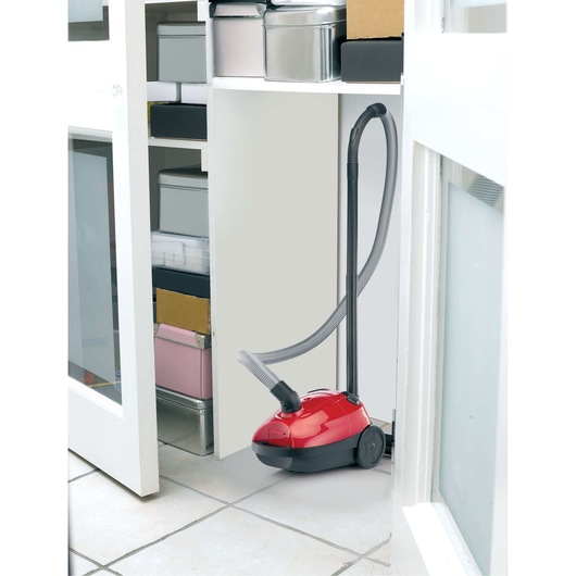 BLACK+DECKER VM1200 red canister vacuum cleaner with hose stored in a white cabinet.