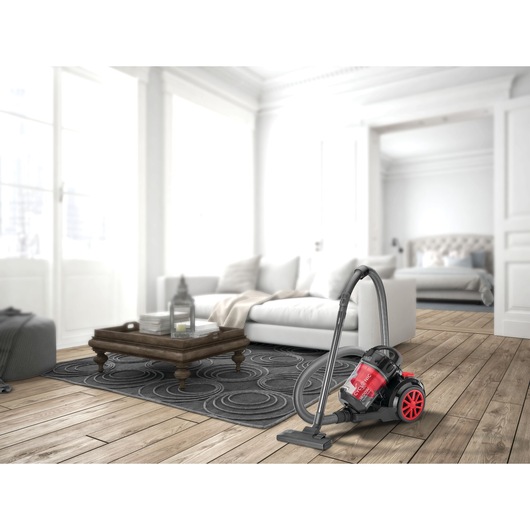 A red and black BLACK+DECKER canister vacuum cleaner model VM1680 is placed on a wooden floor in a bright, modern living room with a white sofa and a coffee table.